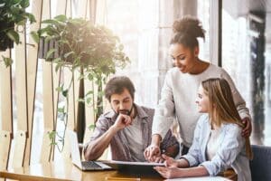 Happy multiracial millennial colleagues discussing company financial statistics at briefing in office, employees brainstorming analyzing growing sales, developing success strategies, reading.