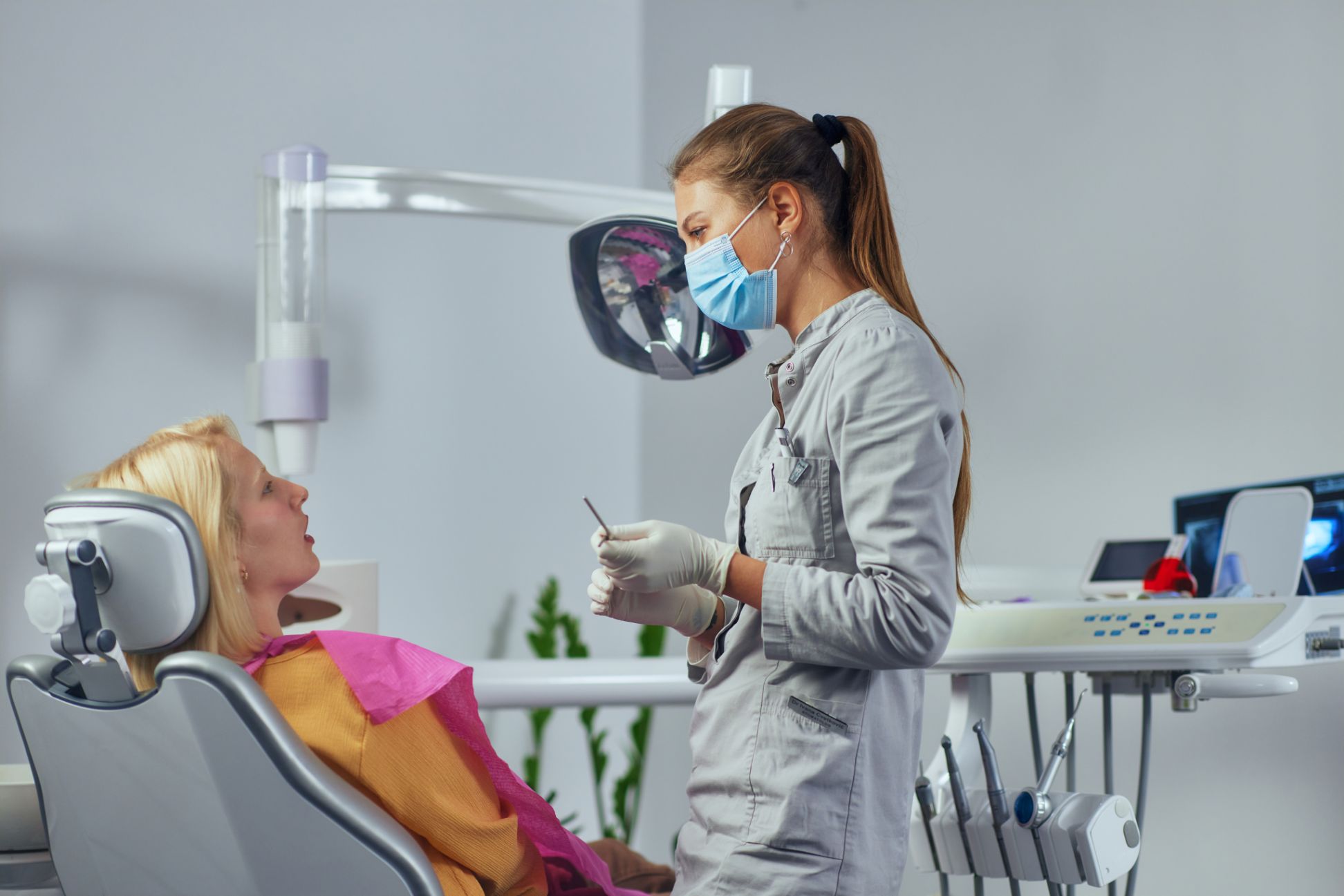 Female patient sitting on dental chair and having conversation with dentist who standing beside her