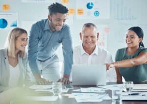 group of 4 people pointing at a computer screen and smiling