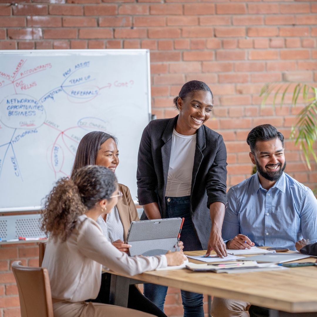 female standing at a table with coworkers pointing at paper