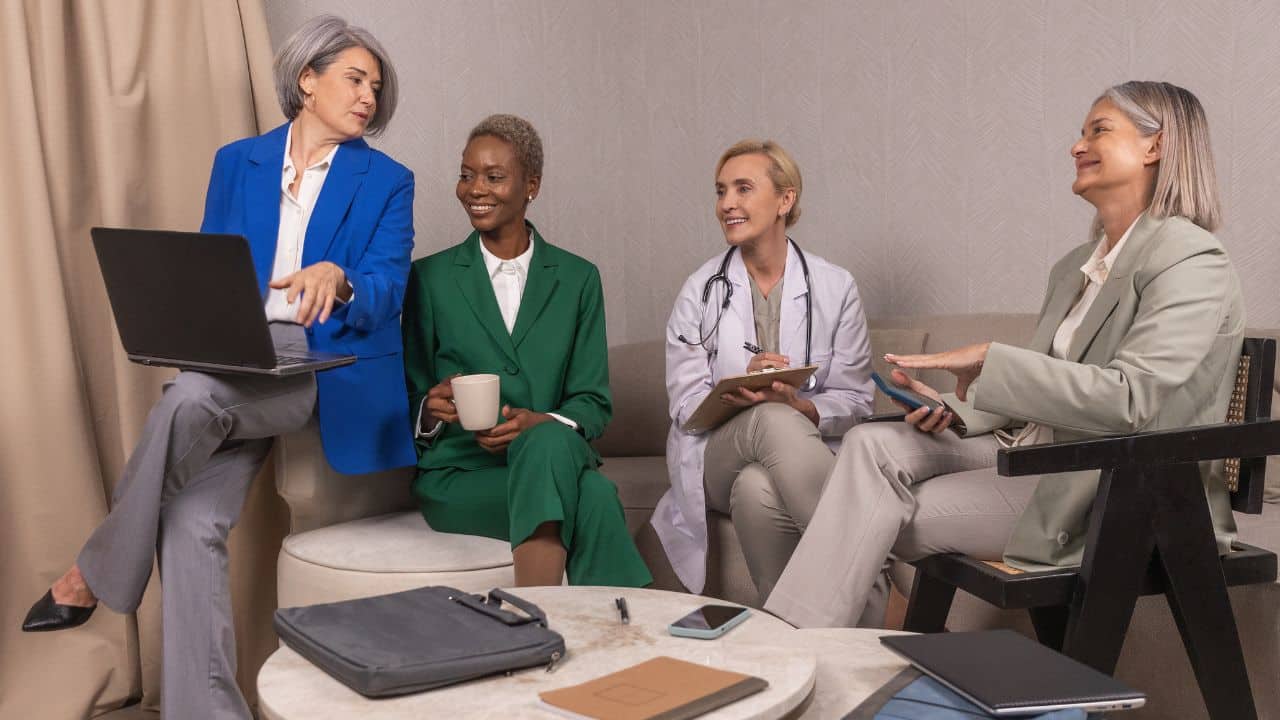 woman in blue suit on laptop presenting to group of three other people, one with stethoscope around necck.