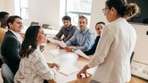 woman at head of table standing speaking with business professionals team