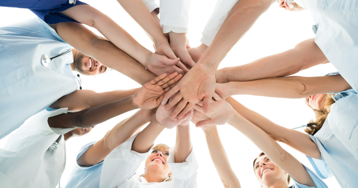 Group of staff at dental practice putting their hands into a pile in sign of unity