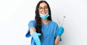 Dentist holding dental tools and extending her hand out to meet new patient