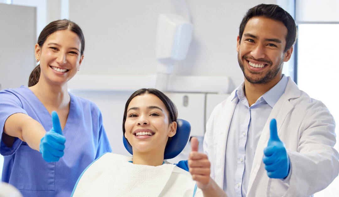 Dentist, dental assistant, and female patient giving photographer thumbs up