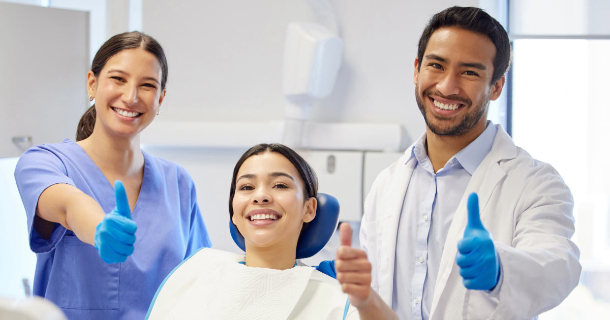 Dentist, dental assistant, and female patient giving photographer thumbs up