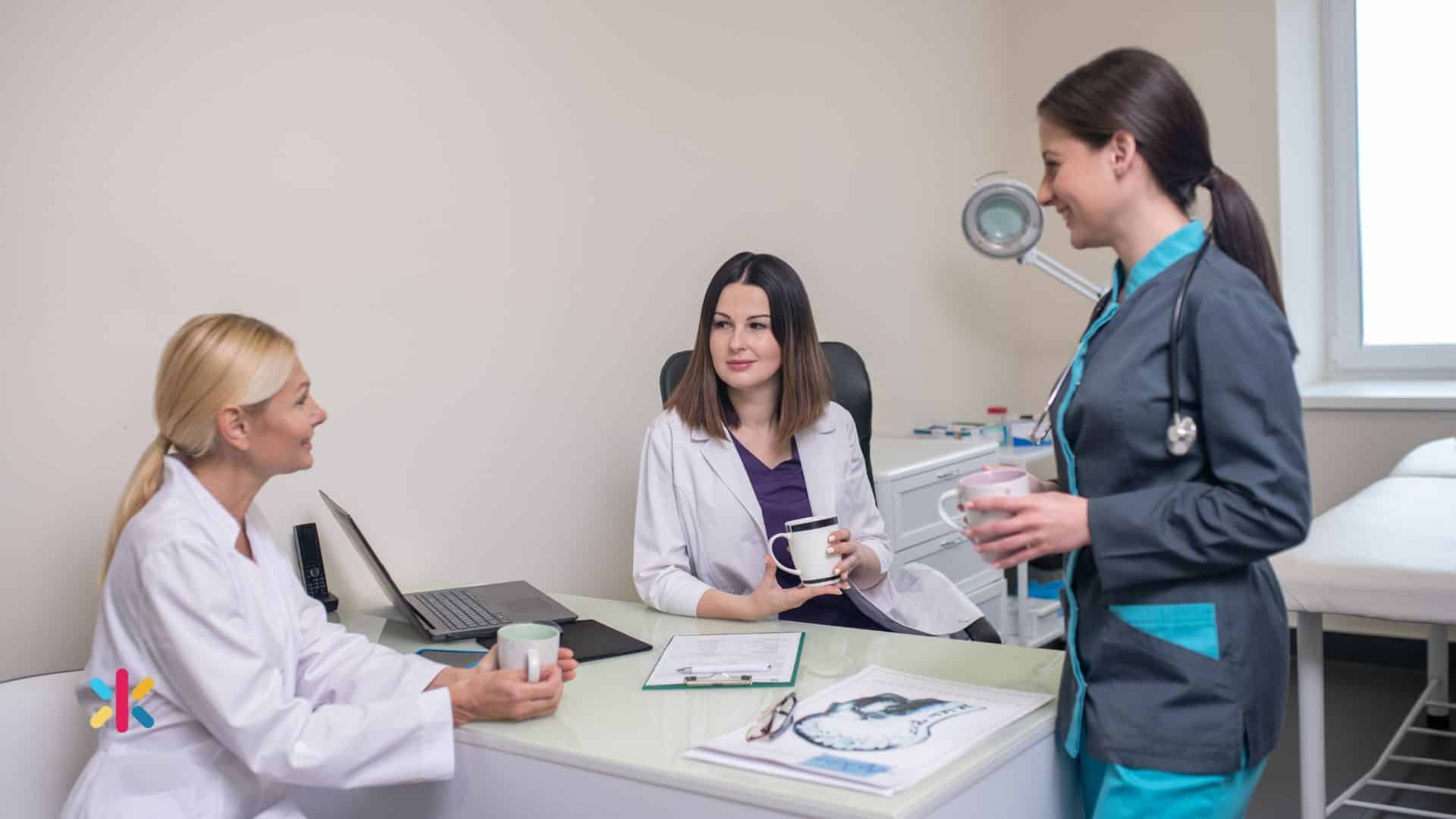 Dental team members talking and reviewing notes in an office setting, holding coffee mugs during a meeting