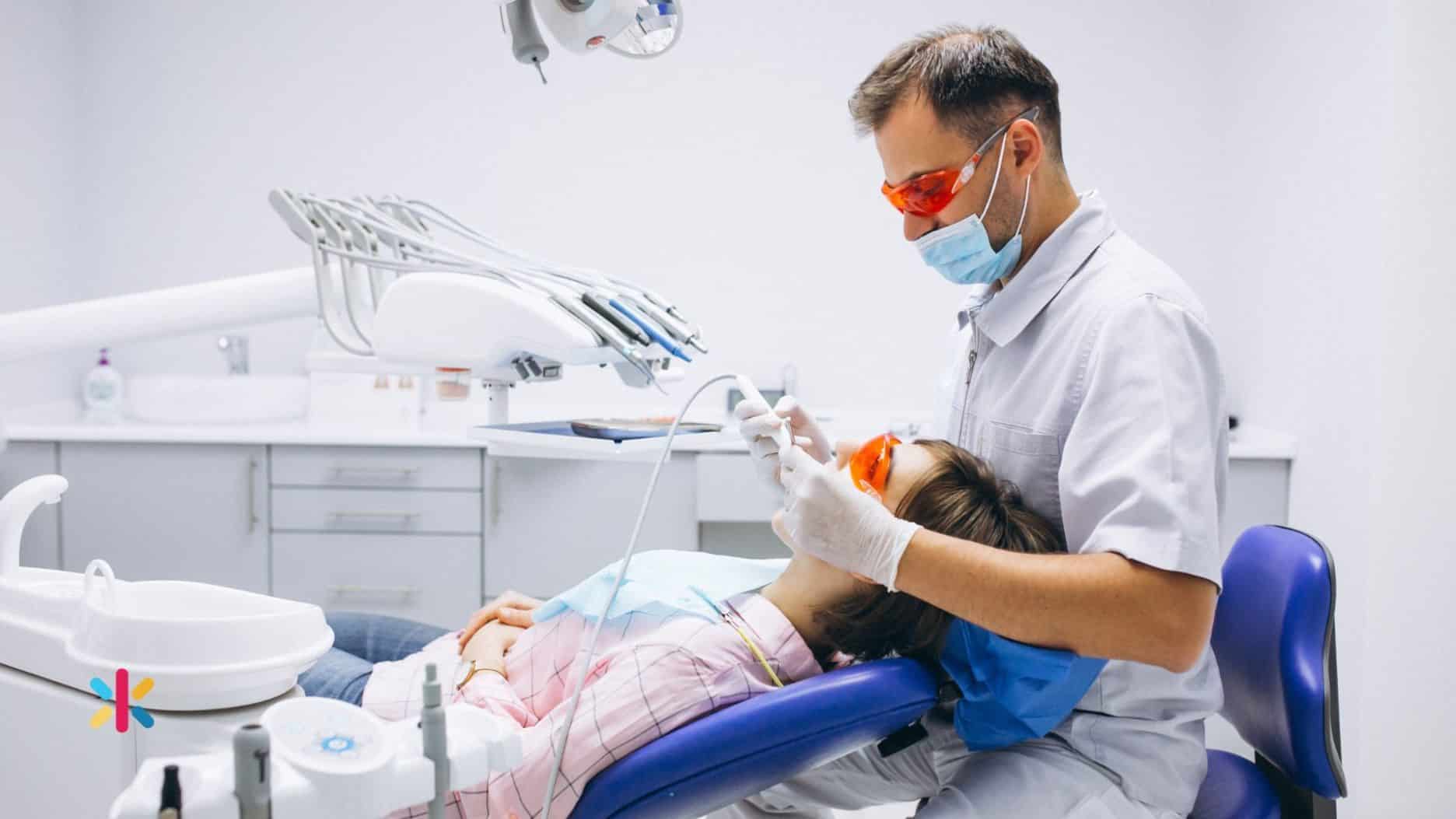 Dentist wearing mask and protective glasses performing a dental procedure on a patient in a treatment chair