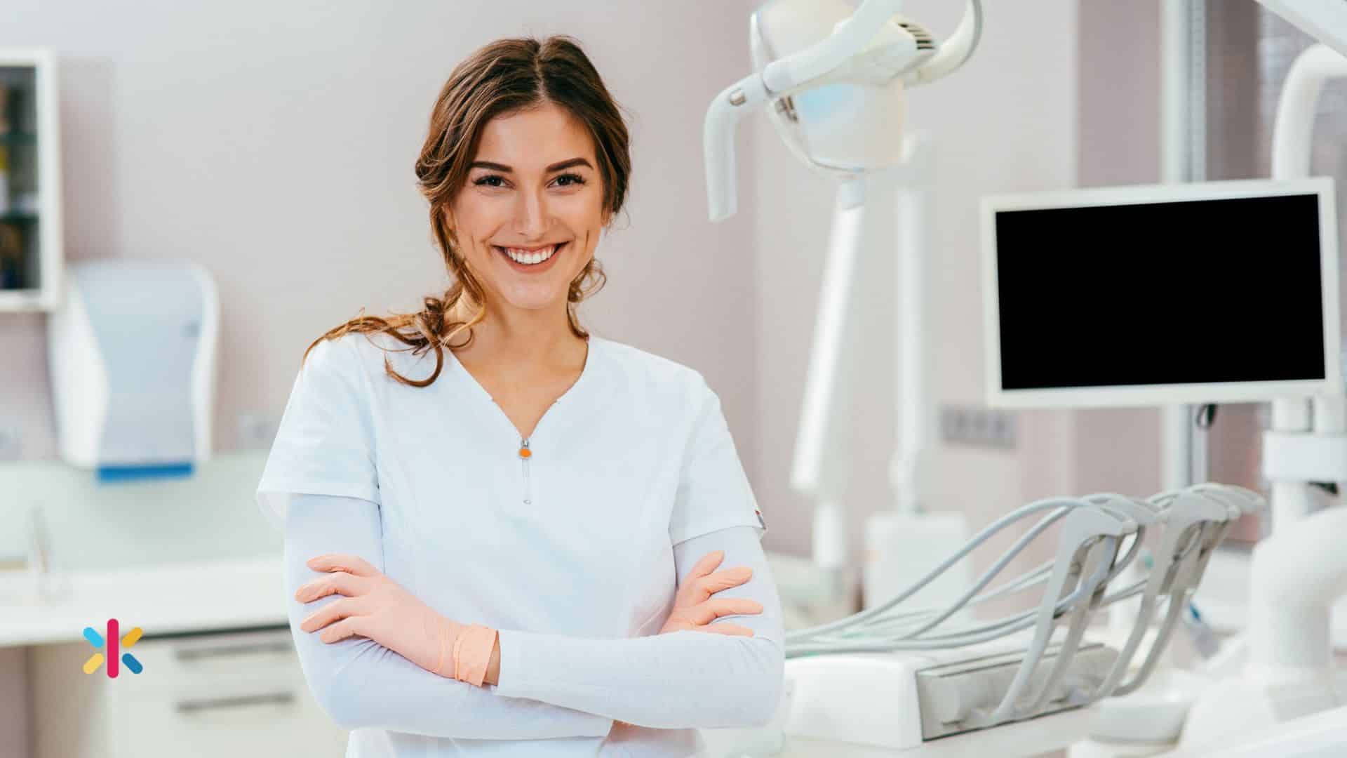 Female dental professional smiling with arms crossed in a modern dental office with equipment in background