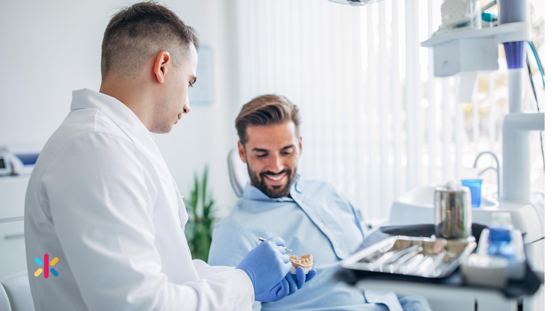 Dentist explaining dental treatment using a tooth model while consulting with a patient in a dental chair.