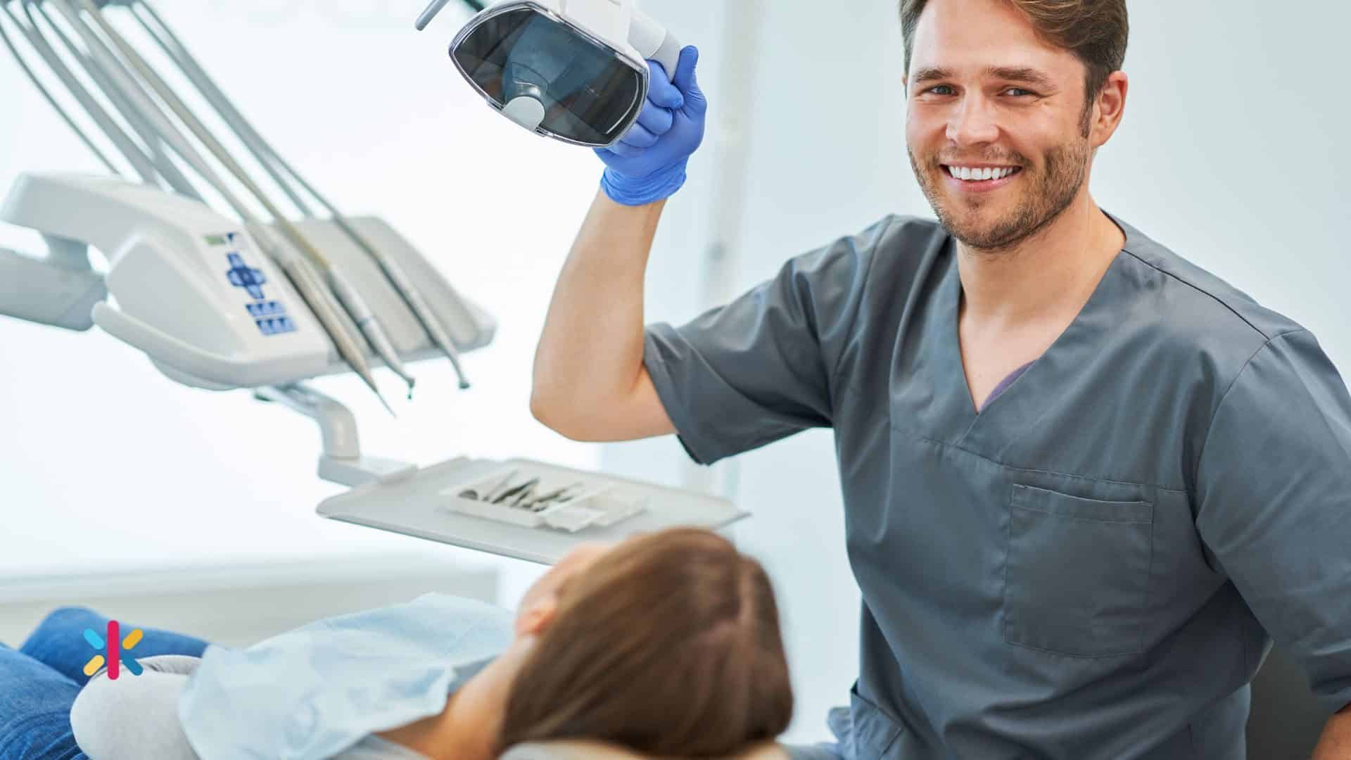 Dentist preparing dental equipment while a patient sits in the dental chair.